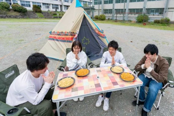 「キャンピース」のグラウンドでキャンプ飯を食べる4人