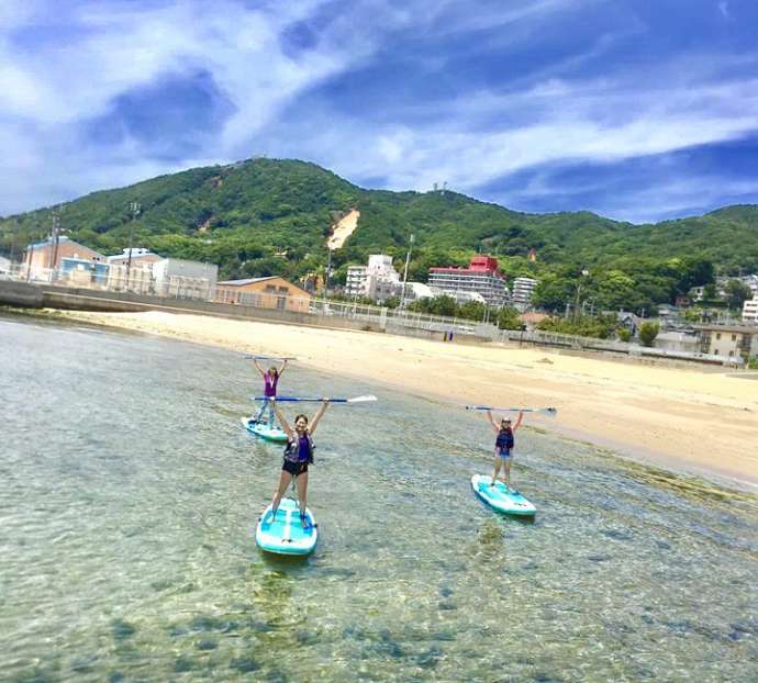 浅瀬の海岸でポーズをとるSUPヨガの参加者たち
