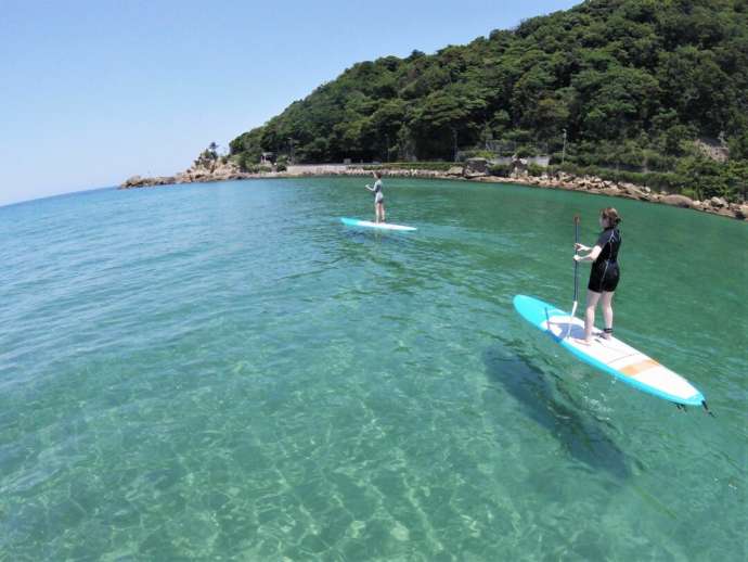夕日ヶ浦海岸の青い海で京丹後135°EASTのSUPを体験する女性たち