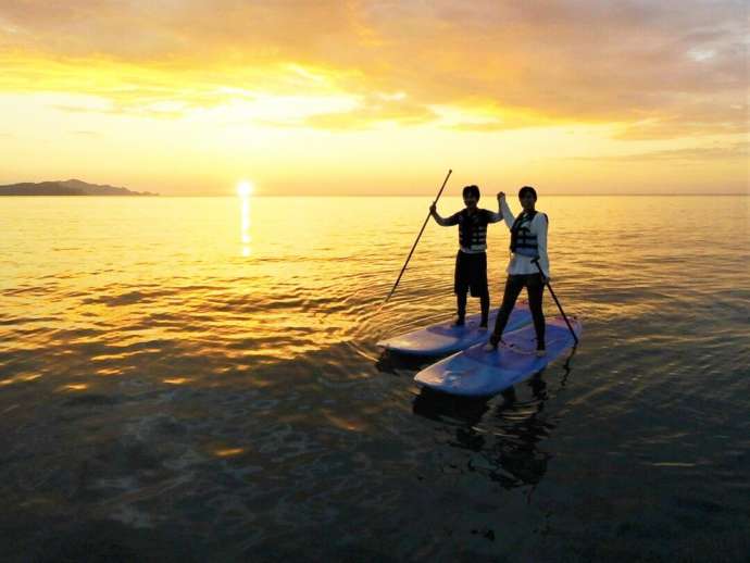 SUPに乗って海上から夕日ヶ浦海岸の夕日を眺める二人