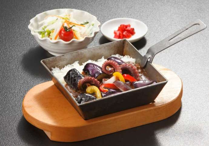 正方形の鉄鍋に入ったカレーとタコやナスが特徴的な鍛冶屋鍋カレー