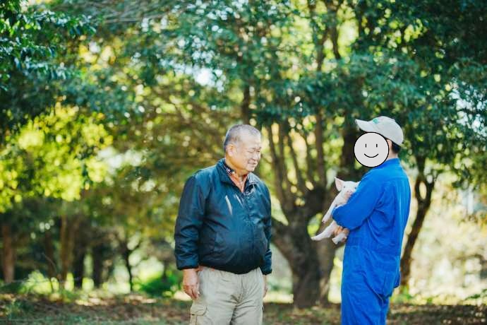 子豚を抱きかかえたスタッフと社長の農山照夫さん