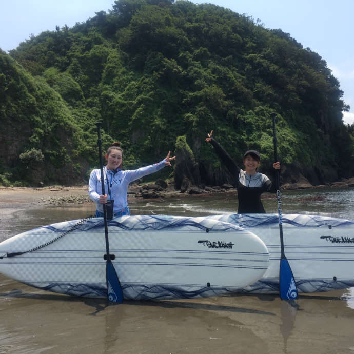 砂浜でSUPボードを前にポーズをとる女性2人
