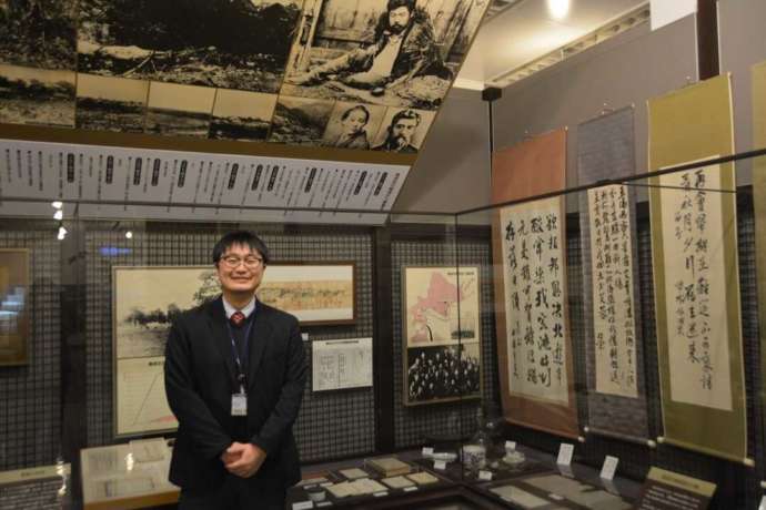 「帯広百年記念館」内に展示される晩成社関連の資料と学芸員の大和田さん(その2)