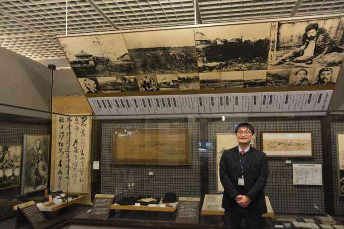 「帯広百年記念館」内に展示される晩成社関連の資料と学芸員の大和田さん(その1)