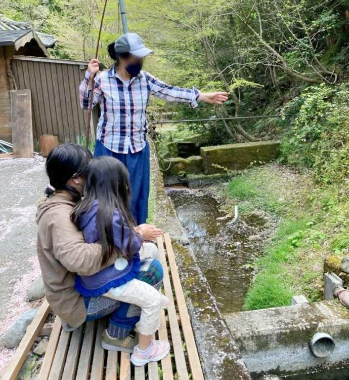「渓流魚料理のお店 醒井楼」前の渓流でニジマスを釣り上げた女性とご家族