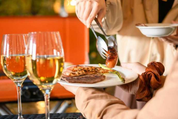 「ホテルソビアル 大阪 ドーム前」のバーベキューでワインを傍らに料理を取り分ける様子