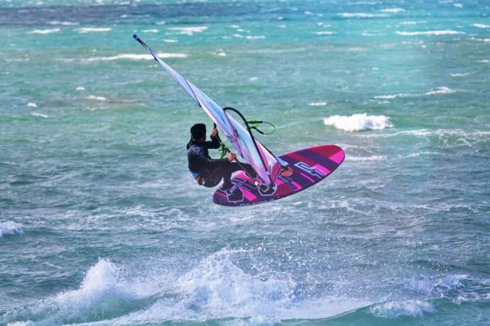 WIND VILLAGEのウインドサーフィン上級者が波しぶきを上げて走っている様子