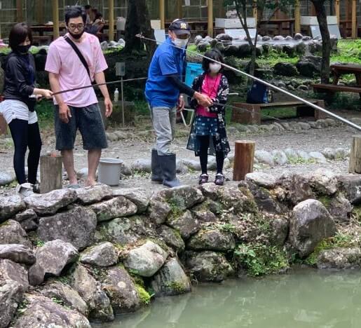 やまめ平でヤマメ釣りを楽しむ利用者とヤマメの釣り方をレクチャーしているスタッフ