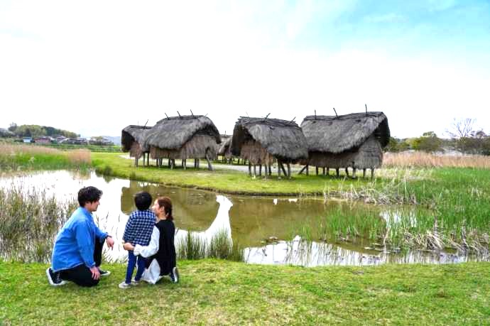 大分県国東市の安国寺集落遺跡公園「弥生のムラ」にある高床建物を引きで眺める家族